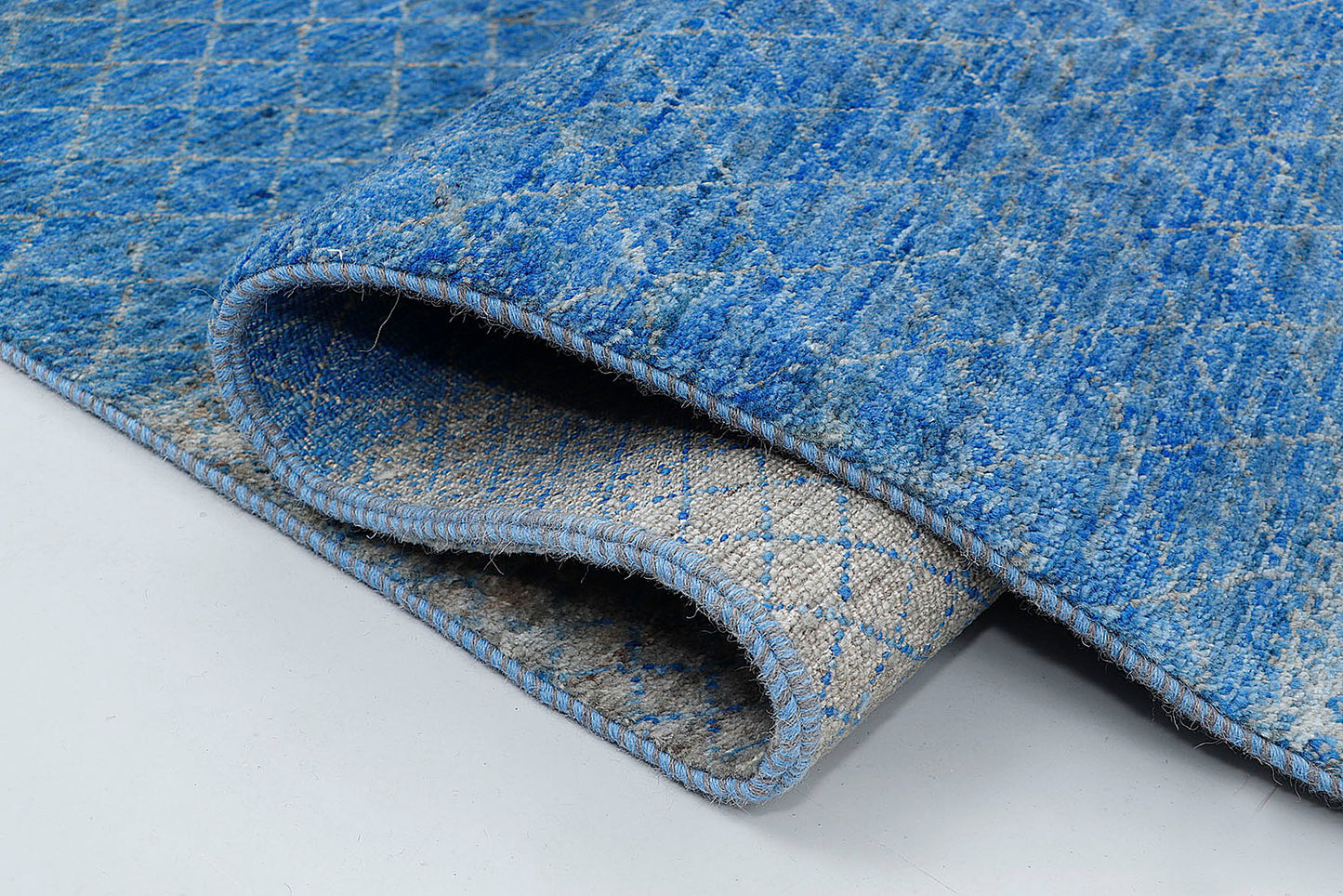 A close-up highlighting the double-knot construction and the unique ombré effect of the blue variegated wool against a shimmering silver background.