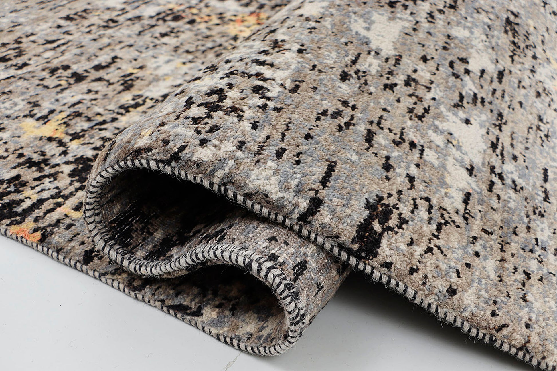 A close-up of a crisp, medium-pile wool rug highlighting the dense, tactile contrast between the dark grey, black, and warm gold hand-knotted yarns in a fractured, painterly effect.