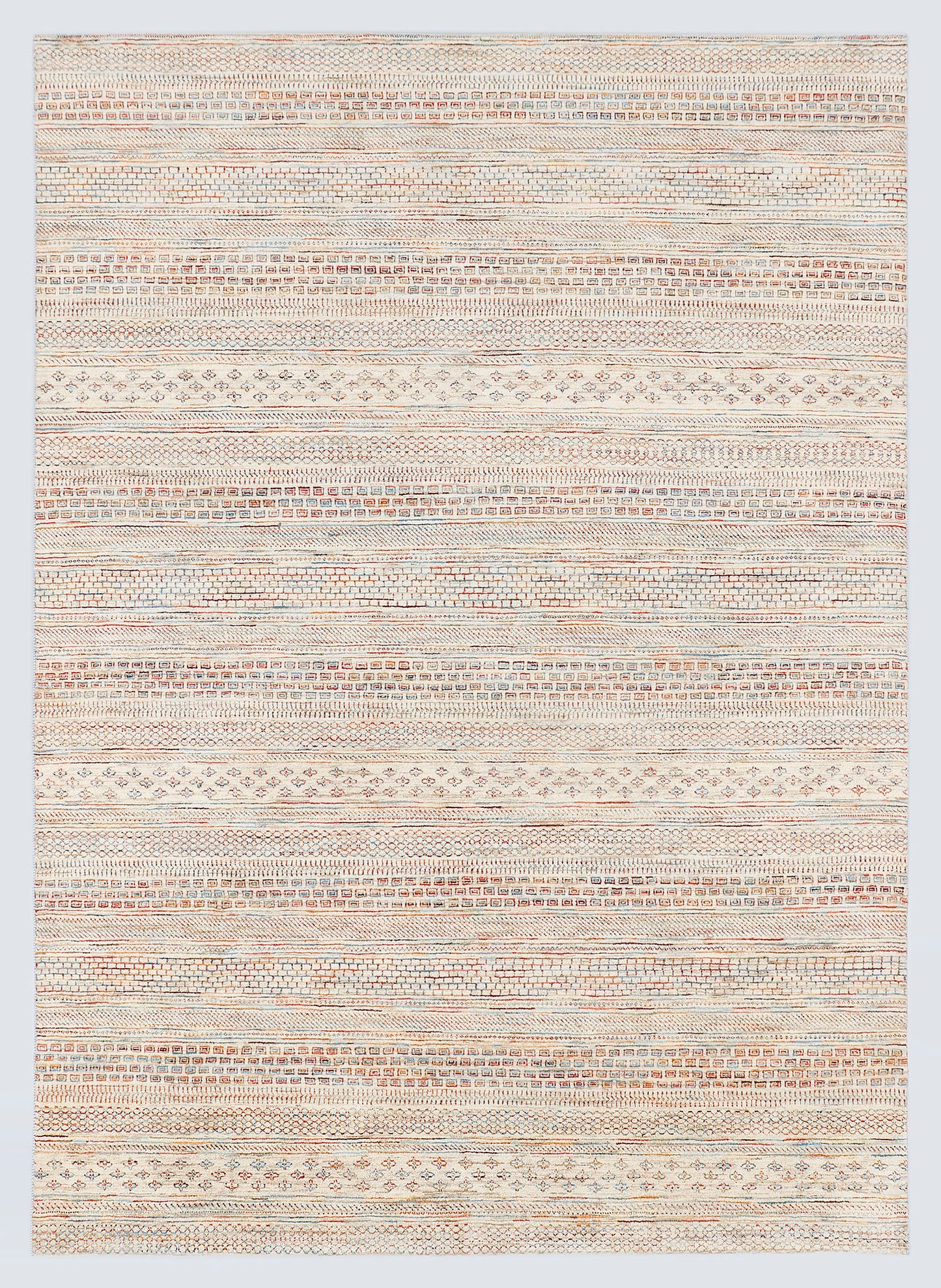 A full view of a hand-knotted wool rug from the Aatish Collection featuring dense horizontal bands of miniature tribal motifs in soft terracotta and powder blue against a luminous ivory foundation.