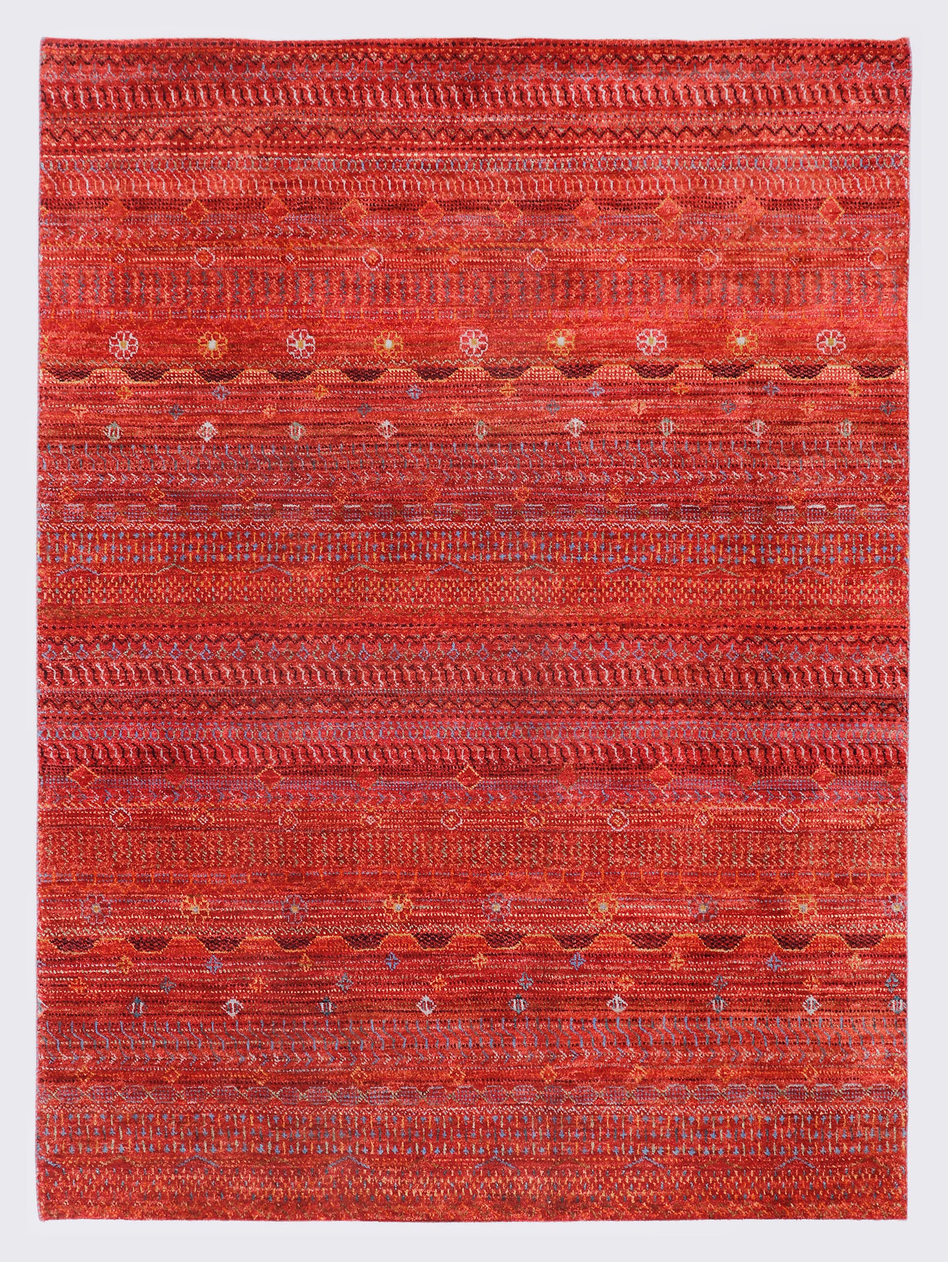 A full view of a vibrant hand-knotted Aatish Gabbeh rug featuring rhythmic horizontal bands of tribal motifs over a saturated red foundation.