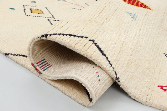 A detailed close-up of a high-pile cream wool rug highlighting the textured knotting of crimson and indigo diamond motifs alongside delicate, ascending chevron tribal lines.