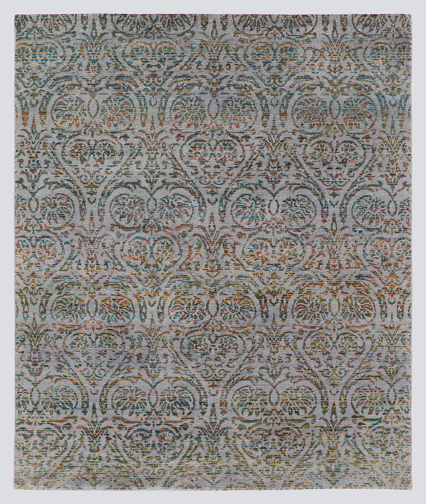 A full view of a modern transitional hand-knotted rug from the Nomad Series, featuring a repeating classical palmette pattern rendered in multi-colored, tie-dyed wool over a silvery-grey foundation.