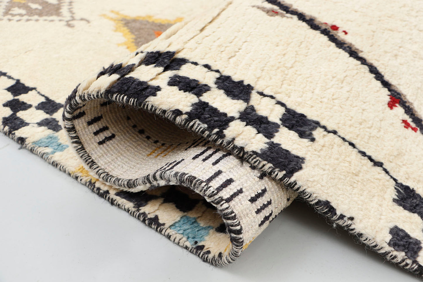A close-up detailing the plush texture of a hand-knotted cream wool rug, highlighting a vibrant terracotta and charcoal geometric triangle alongside a section of the black and white checkerboard border.