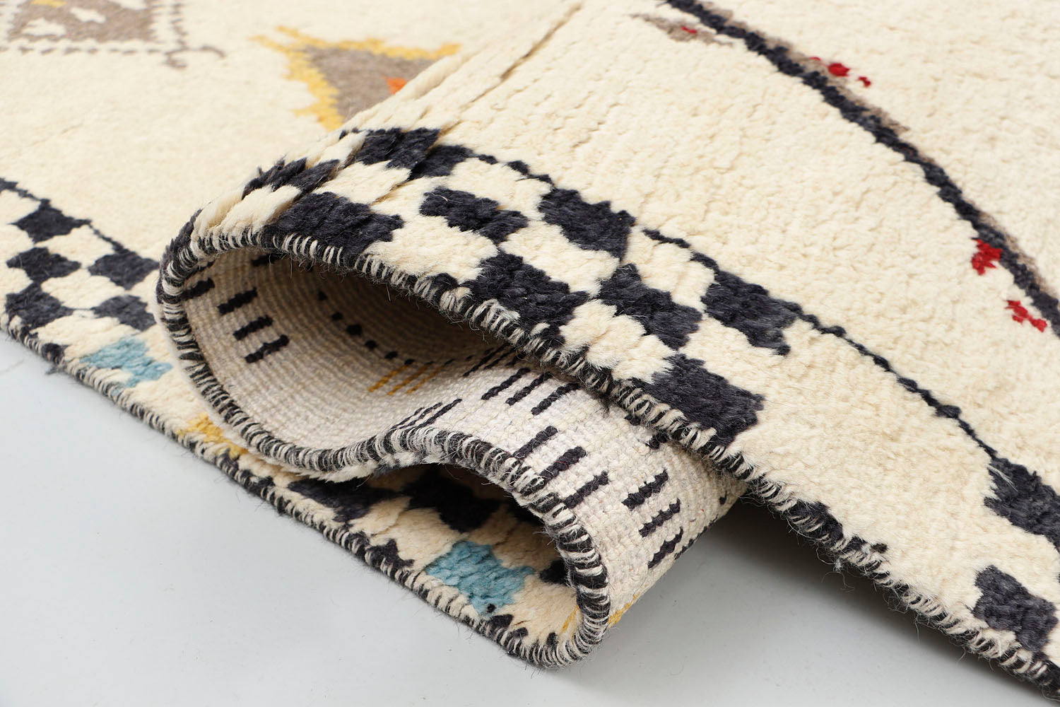 A close-up detailing the plush texture of a hand-knotted cream wool rug, highlighting a vibrant terracotta and charcoal geometric triangle alongside a section of the black and white checkerboard border.